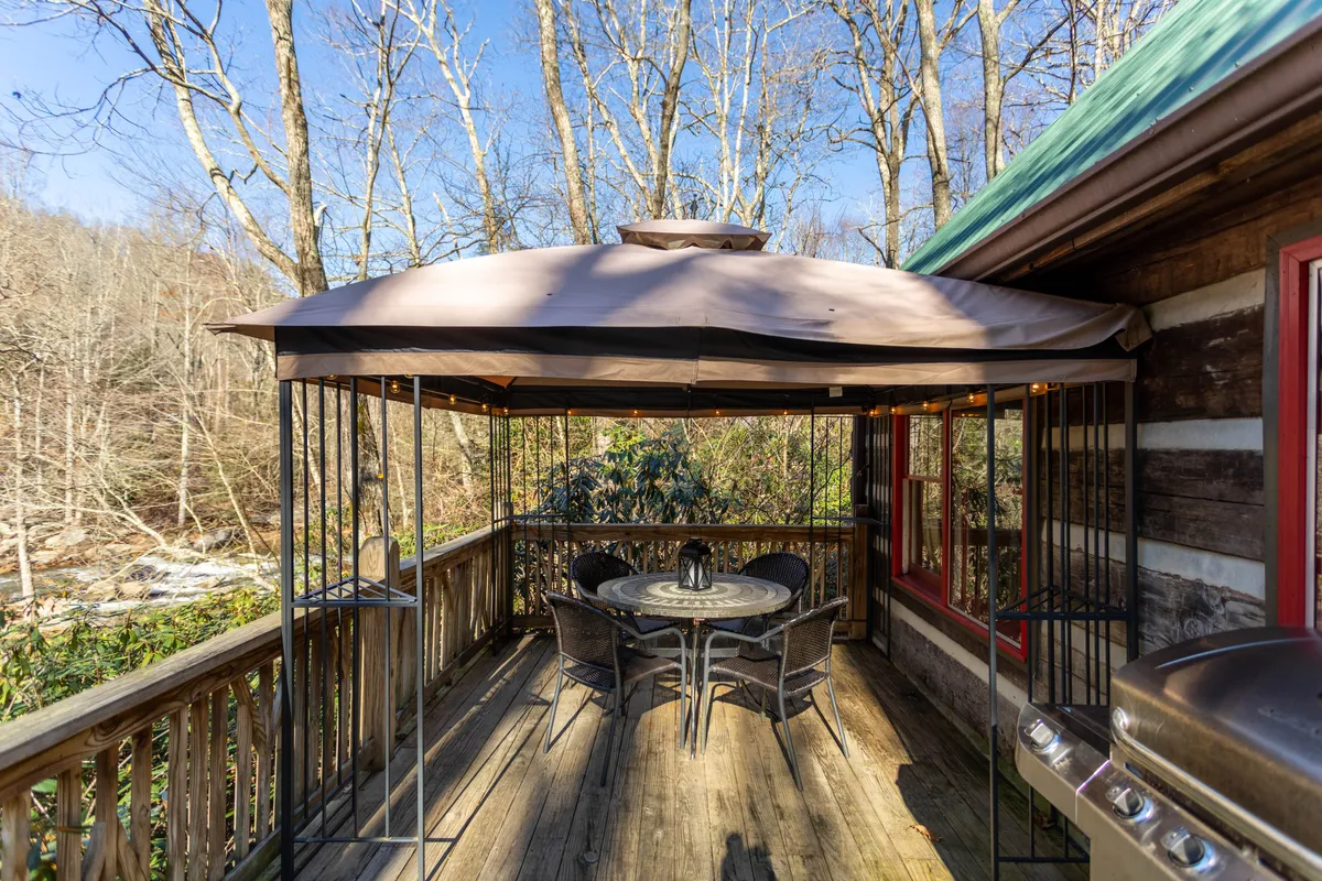 An inviting outdoor gazebo and dining area set among tall trees, with a table ready for gatherings and relaxation. The tranquil setting enhances the sense of outdoor living and connection to nature, while the large yard area is visible, suggesting space for play and wildlife watching.