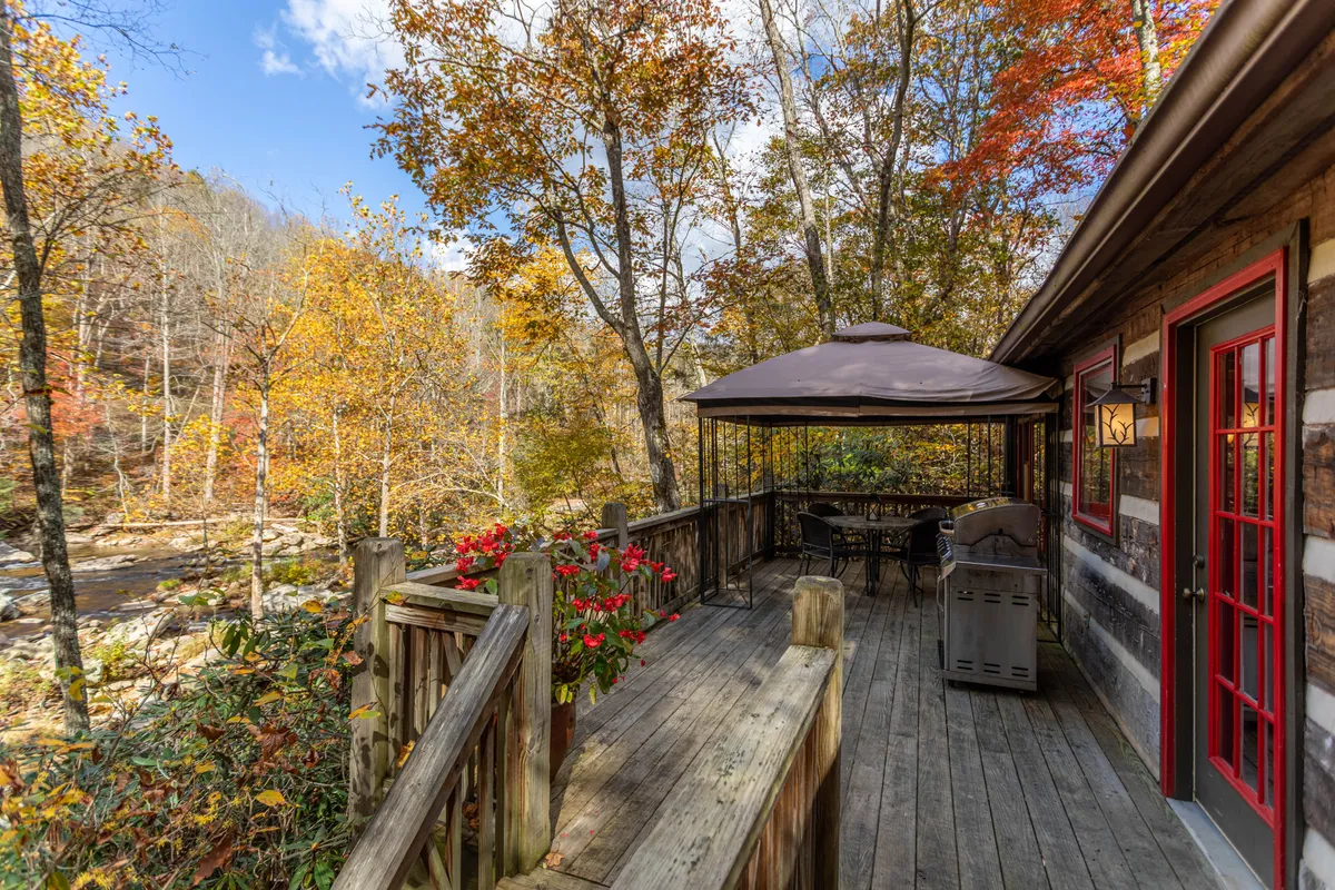 A picturesque riverside deck with a wooden dining set, gazebo, and sweeping views of the river and autumn foliage. The setting exudes tranquility and is perfect for al fresco meals, relaxing in mountain air, or enjoying coffee at sunrise and dinner at sunset.