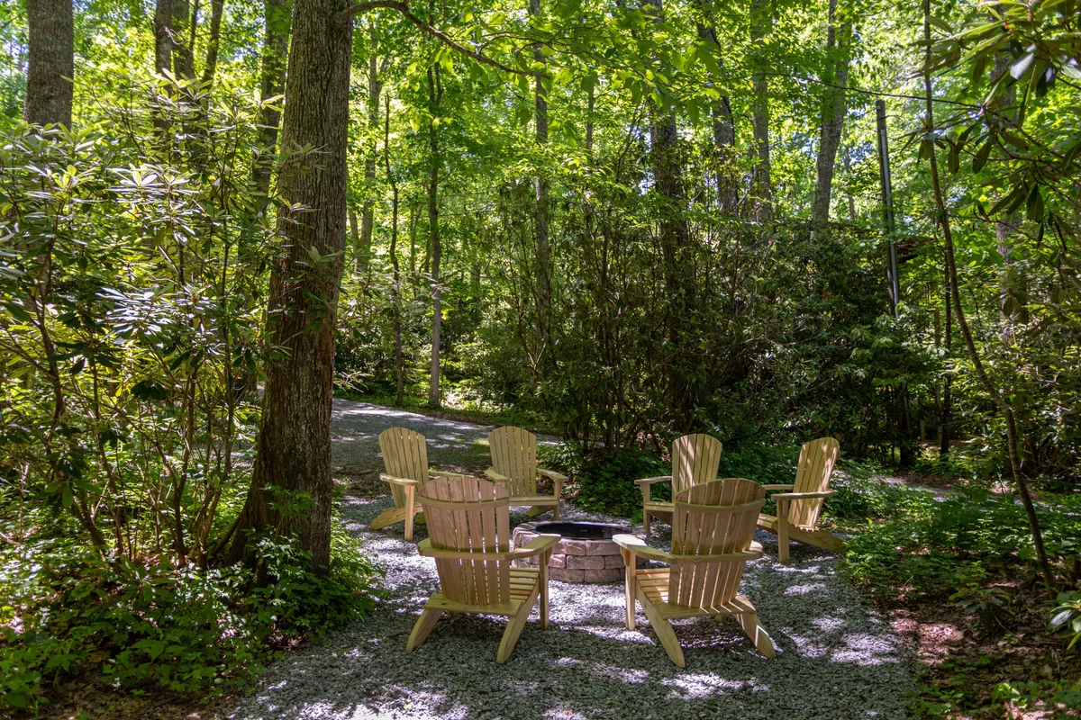 This exterior image captures a welcoming fire pit surrounded by Adirondack chairs set amidst lush greenery. The setup suggests an inviting space for group gatherings, storytelling, and enjoying evenings outdoors under the stars.