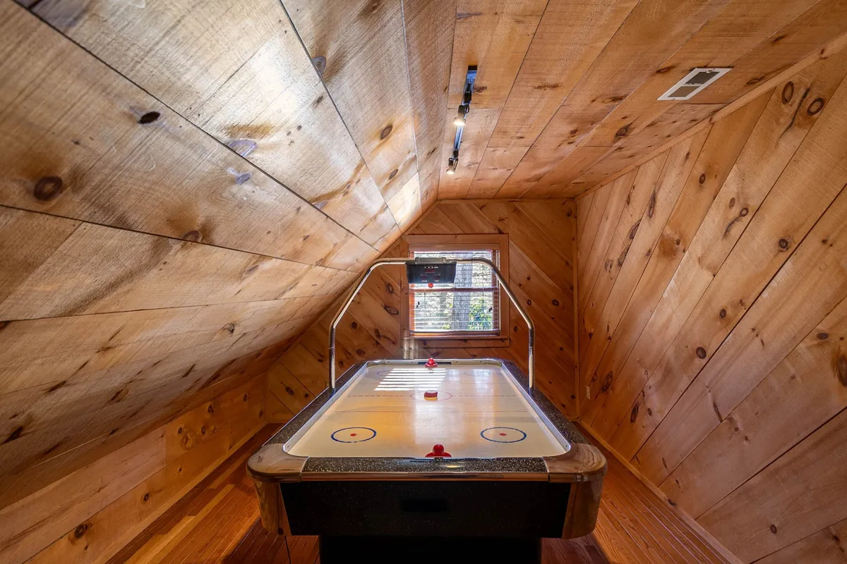 A playful game room with an air hockey table, rustic wooden walls, and a window bringing in natural light. The space is lively and inviting, tailored for group fun and providing flexibility for kids or extra guests as described in the narrative.