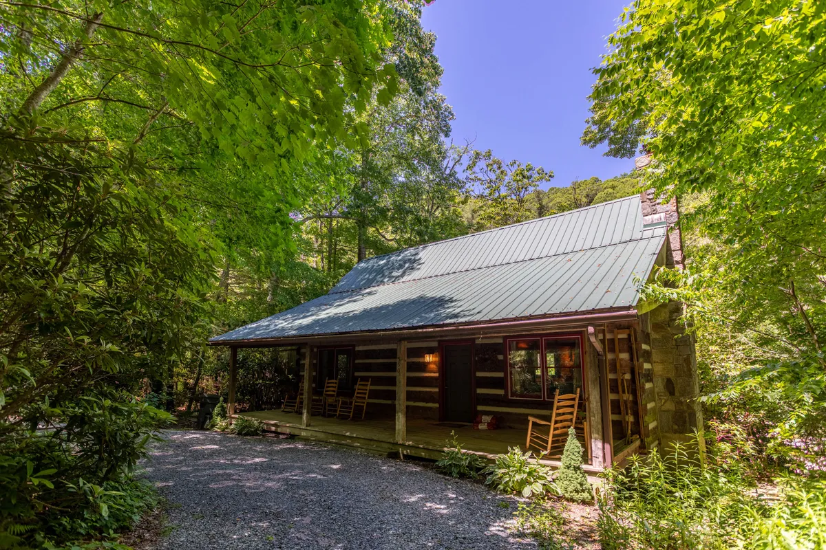 This image showcases the exterior of a classic log cabin nestled among lush green foliage. The inviting porch is outfitted with rocking chairs, indicating a perfect spot to unwind after a day of adventure. The serenity and lushness of the setting reflect the tranquil mountain environment.