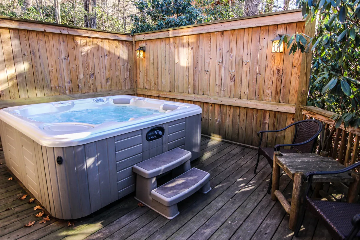 This image shows a spacious wooden deck with an inviting hot tub surrounded by lush greenery. Nearby, comfortable outdoor chairs encourage relaxation while the river’s presence can be felt in the tranquil setting. The ambiance is serene, ideal for both daytime and nighttime enjoyment, with the hot tub as a focal point.