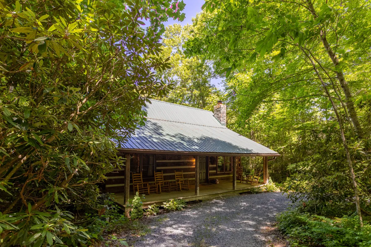 A classic log cabin with a spacious front porch featuring rocking chairs, all set in a tranquil, green environment. The scene hints at relaxation, porch chats, and connection to the natural world right outside the door.