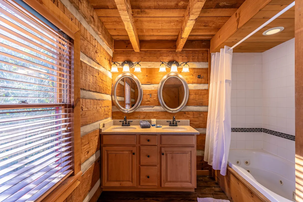 A warm, tranquil bathroom featuring a double granite vanity with mirrors, a soaking bathtub, and wood-paneled walls. The space is illuminated by soft natural light, creating a spa-like ambiance ideal for relaxation.