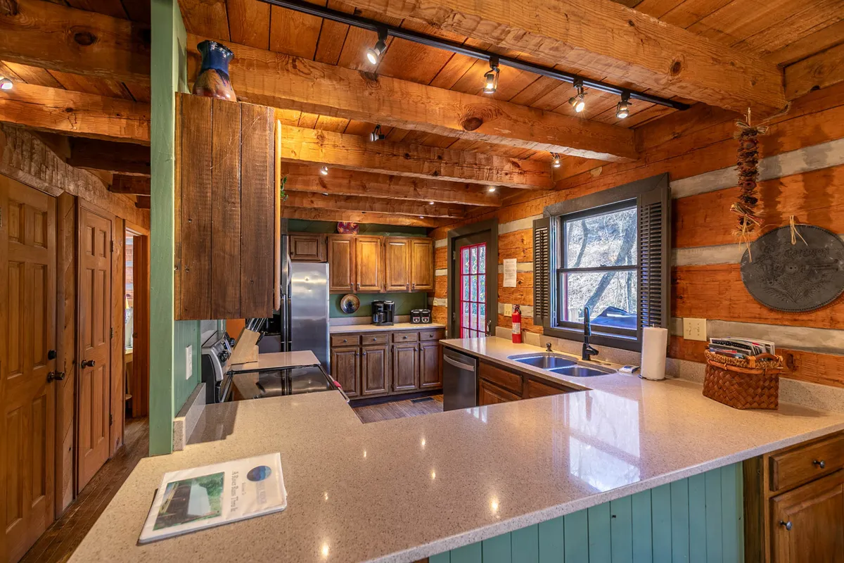 A modern kitchen featuring prominent wooden beams, a kitchen island, high-end appliances, and large windows that let in natural light. The scene radiates warmth, with space for both cooking and gathering, emphasizing the kitchen’s role as a central hub for both everyday moments and special occasions.